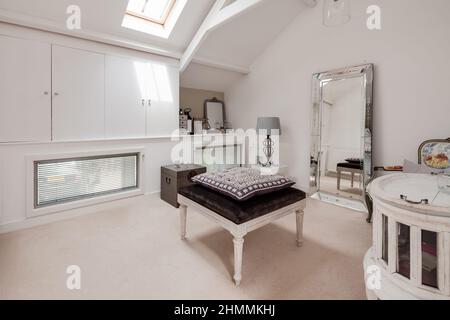 Newport, Essex - 10 2018 juillet : dressing chic de luxe lumineux et éclairé au soleil, décoré simplement dans des tons de blanc avec placards, tabouret et miroir intégrés Banque D'Images