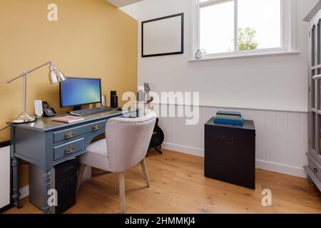 Newport, Essex - juillet 10 2018: Bureau moderne de luxe décoré en jaune et blanc avec bureau, chaise et ordinateur Banque D'Images