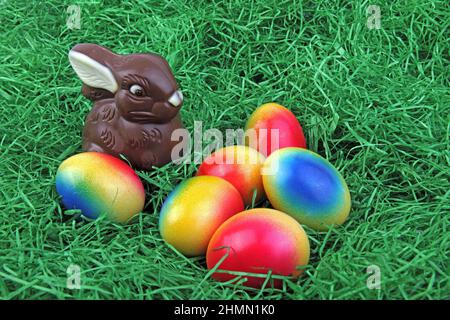 Lapin de Pâques au chocolat avec œufs de Pâques aux couleurs vives sur l'herbe Banque D'Images
