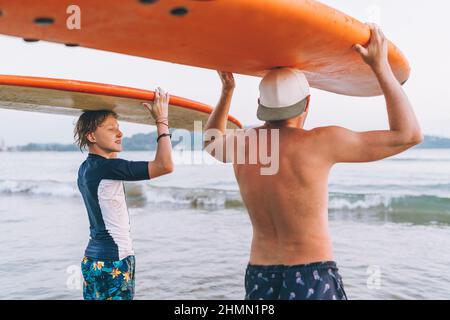 Jeune garçon avec son père avec des planches de surf sur la tête marchant dans les vagues sur la plage d'Udawalawe au Sri Lanka.Vacances actives en famille ou sport actif pe Banque D'Images