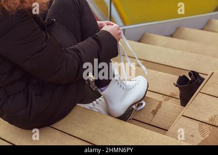 Une jeune femme met des patins à glace sur ses pieds, assise sur des marches en bois. Banque D'Images