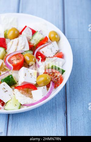 Salade grecque. Cuisine grecque traditionnelle. Nourriture végétarienne saine. Légumes frais et fromage feta dans une assiette blanche. Gros plan, fond bleu. Banque D'Images