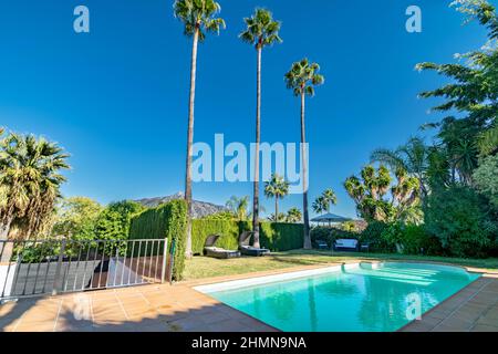 Une image au bord de la piscine dans une villa à Marbella avec des palmiers et des montagnes en arrière-plan Banque D'Images