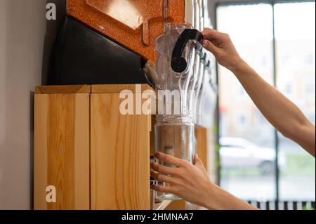 Une femme remplit un pot de lentilles rouges. Vendre des produits en vrac en poids dans un éco-magasin. Concept commercial sans emballage plastique Banque D'Images
