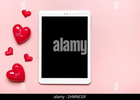 Tablette pour choisir des cadeaux, fait l'achat, deux coeurs rouges sur table rose vue du dessus plat Lay liste d'achats de vacances, bonne Saint-Valentin, fête, en ligne Banque D'Images