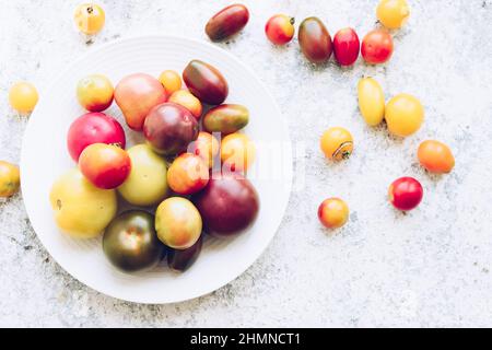 Différentes tomates colorées sur plaque blanche sur table en pierre. Différents types de tomates fraîches bio sur fond de béton gris avec place pour le texte. Ferme Banque D'Images