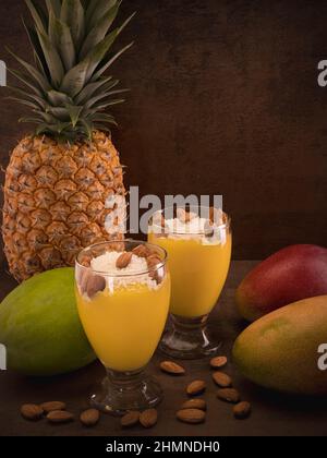 La photo montre un dessert de mangue sain. En outre, plusieurs mangues et ananas sont présentés. Les poignées d'amandes peuvent être vues sur une ta en bois Banque D'Images