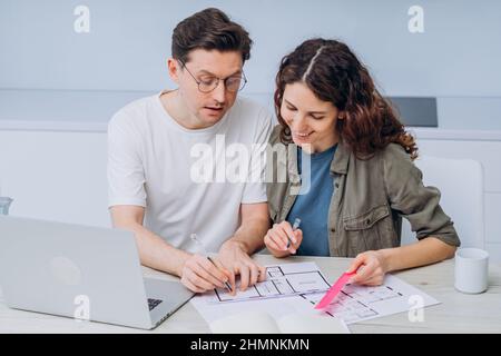 Le couple est assis dans la cuisine boissons café pour le petit-déjeuner et parle de dessins de rénovation d'appartement faire des notes dans l'ordinateur portable et le bloc-notes Banque D'Images