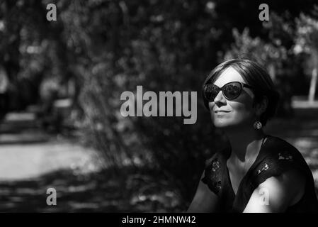 Portrait d'une femme blanche de 30 ans, assise avec son visage au soleil dans l'ombre des arbres Banque D'Images