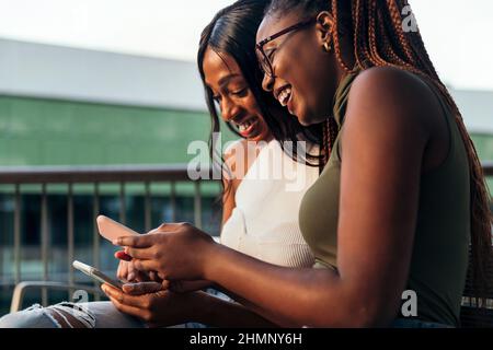 deux jeunes femmes noires rient heureusement en consultant leurs téléphones mobiles, concept de jeunesse et de communication, copier l'espace pour le texte Banque D'Images