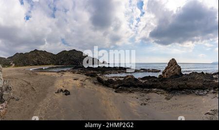 Une vue panoramique sur une plage de sable isolée sur une côte montagneuse sauvage avec des rochers Banque D'Images