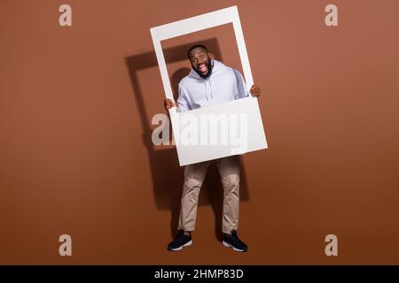 Photo d'impressionne un gars étonnant vêtu d'un sweat-shirt blanc tenant un cadre photo isolé couleur marron fond Banque D'Images