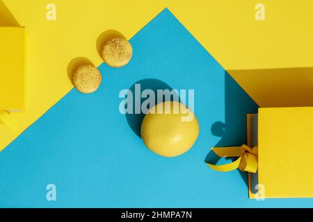 Boîte cadeau jaune printemps avec noeud en ruban, pamplemousse jaune et deux macarons français sur fond jaune et bleu. Salutation pour International Women's Banque D'Images