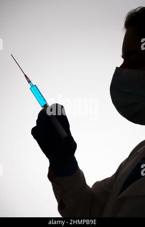 Silhouette d'un médecin avec une seringue remplie de liquide bleu. Concept de vaccination. Banque D'Images