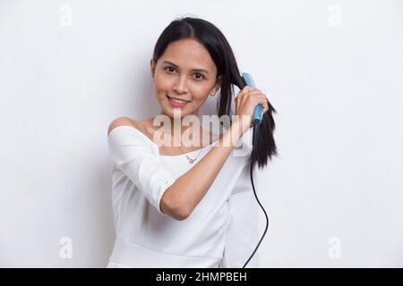 jeune asiatique belle femme heureuse lissant les cheveux avec un lisseur sur fond blanc Banque D'Images