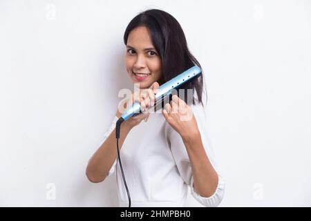 jeune asiatique belle femme heureuse lissant les cheveux avec un lisseur sur fond blanc Banque D'Images