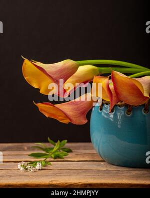 Vase d'orange Calla Lilies sur une table en bois Banque D'Images