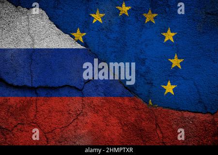 Photo plein cadre d'un drapeau abîmé de la Russie et de l'Union européenne (UE) peint sur un mur fissuré. Banque D'Images