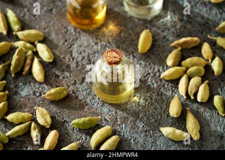 Bouteille d'huile essentielle avec graines de cardamome sur fond sombre Banque D'Images