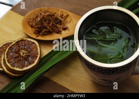 Goias, Brésil – 11 février 2022 : une tasse de thé, avec des feuilles de citronnelle, quelques tranches d'orange déshydratée, une cuillère avec des herbes. Banque D'Images
