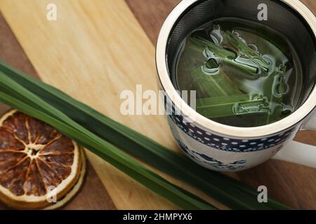 Goias, Brésil – 11 février 2022 : une tasse de thé, avec des feuilles de citronnelle et des tranches d'orange déshydratées, sur une surface en bois. Banque D'Images