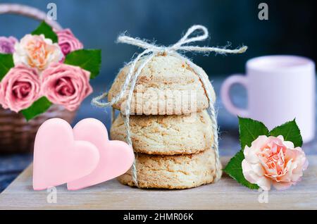 Biscuits aux flocons d'avoine sur une planche en bois, des coeurs en chocolat et une fleur de rose, sur fond bleu défoqué avec un panier de roses. Attention sélective Banque D'Images