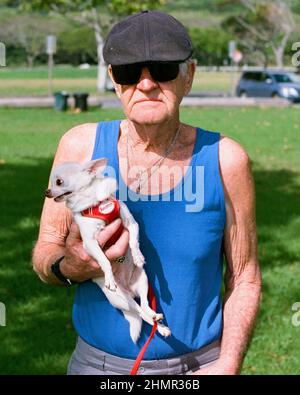 Vieil homme avec un chapeau et des lunettes de soleil tenant un chien chihuahua Banque D'Images
