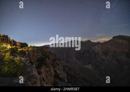 Ciel nocturne rempli d'étoiles au-dessus des falaises spectaculaires et des montagnes de Jebel Akhdar, Oman, avec des lumières de station balnéaire à flanc de falaise illuminant le paysage accidenté Banque D'Images