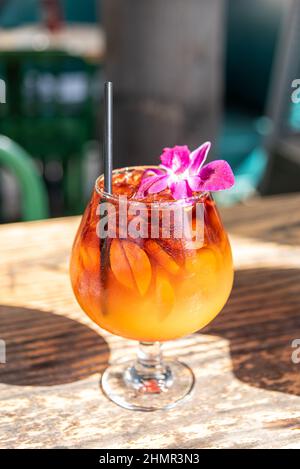 Plan vertical d'une glace froide Delicious Mai Tai avec une fleur et une paille sur une table en bois Banque D'Images