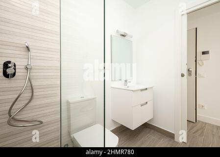 Salle de bains avec douche à parois de verre, meuble lavabo blanc et miroir intégré sans cadre dans l'appartement de location Banque D'Images