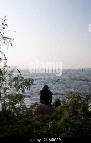 Silhouette d'homme assis sur le rocher, pêche au coucher du soleil Banque D'Images