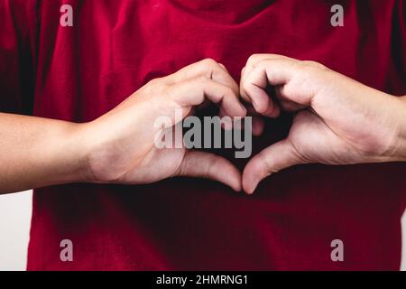 La personne montre des mains signe d'amour près de la poitrine. L'homme avec une chemise rouge en gros plan moyen. Banque D'Images