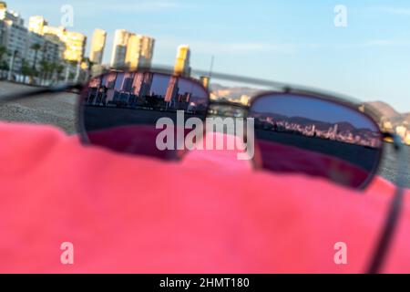 Lunettes de soleil vue sur Benidorm dans une serviette rouge. Sur la plage de Poniente, les tours de la ville ont été vues à travers des lunettes de soleil teintées posées dans une heure d'or. Banque D'Images