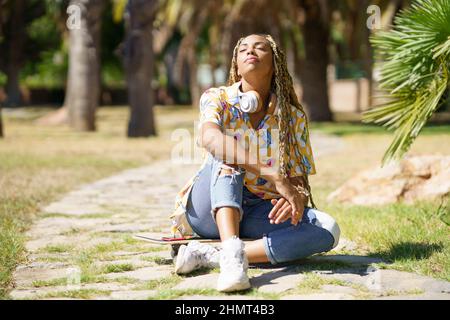 Femme africaine avec planche à roulettes se détendre après avoir fait de l'équitation avec les yeux fermés. Banque D'Images