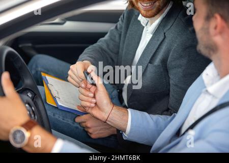 Le vendeur remet les clés de la nouvelle voiture au client dans une atmosphère agréable à la boutique d'auto. Voiture, boutique, achat Banque D'Images