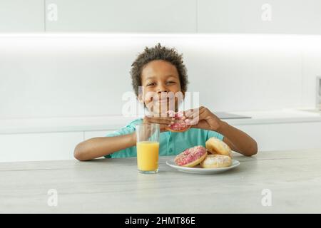 Portrait d'un enfant garçon heureux qui boit du jus d'orange et mange des beignets Banque D'Images