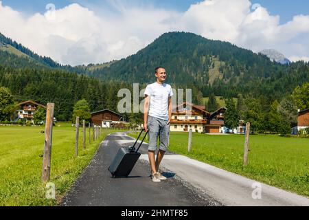 Voyageur homme marchant avec une valise dans la rue dans les montagnes. Concept de voyage. Banque D'Images