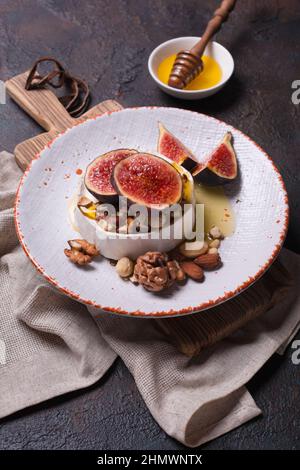 Hors-d'œuvre gastronomique de brie blanc ou de camembert avec figues fraîches, noix et miel sur fond de béton foncé Banque D'Images