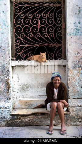 La femme cubaine est assise sur la marche avant de sa maison avec son chat de tabby de couleur orange. Banque D'Images