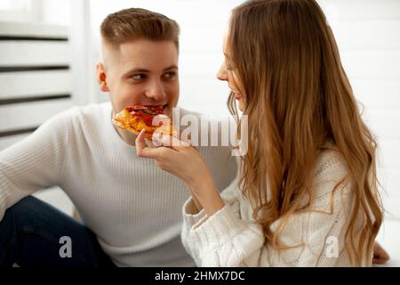 Relation romantique de jeune couple amoureux. Belle femme aux cheveux longs bruns alimente sa pizza d'ami, elle leur donne un grand plaisir. Concept Banque D'Images