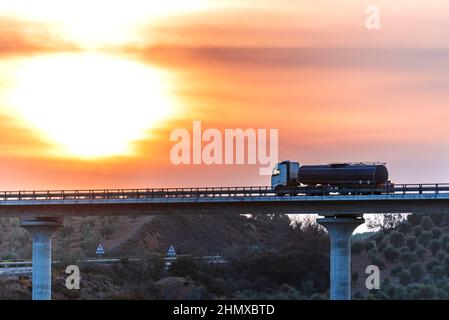 Camion-citerne avec des marchandises dangereuses circulant sur un pont au coucher du soleil. Banque D'Images