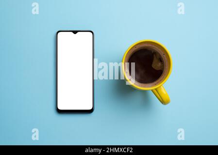 Maquette de téléphone et tasse à café sur une surface bleue propre. Vue de dessus, composition de la pose à plat. Smartphone avec écran blanc et isolé pour la présentation des applications Banque D'Images