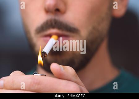 Gros plan de jeune homme éclairant la cigarette avec l'allume-cigare. Tabagisme et dépendance à la nicotine Banque D'Images