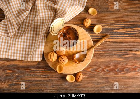 Boîte de conserve avec du lait concentré bouilli et de savoureux biscuits en forme de noix sur fond de bois Banque D'Images