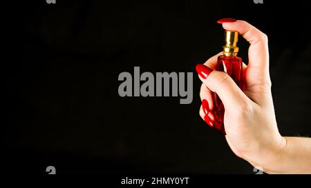 Crop personne avec flacon de parfum. Crop anonyme personne démontrant bouteille dorée avec parfum sur fond noir. Banque D'Images