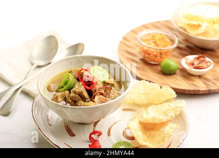 Soupe de bœuf indonésienne Soto Daging, servie sur un bol en céramique avec Krupuk Melinjo, Sambal et Lime Banque D'Images