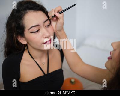 Une jeune femme faisant le maquillage crayon pour sourcils à son amie femelle sur halloween Banque D'Images