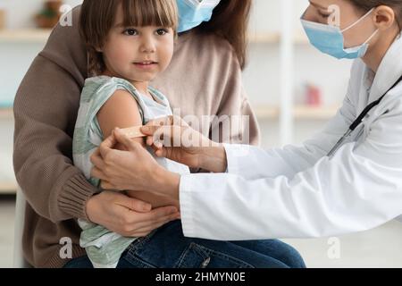 Femme médecin mettant du plâtre médical dans le bras du patient de garçon après l'injection de vaccination contre le covid-19 pendant une pandémie Banque D'Images