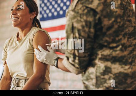 Une femme de souche reçoit une dose du vaccin Covid-19 dans l'hôpital militaire. Une militaire américaine souriant avec joie tout en se faisant injé Banque D'Images