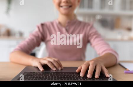 Heureux mignon européen adolescente dactylographiant sur ordinateur portable clavier dans la cuisine intérieure, flou Banque D'Images